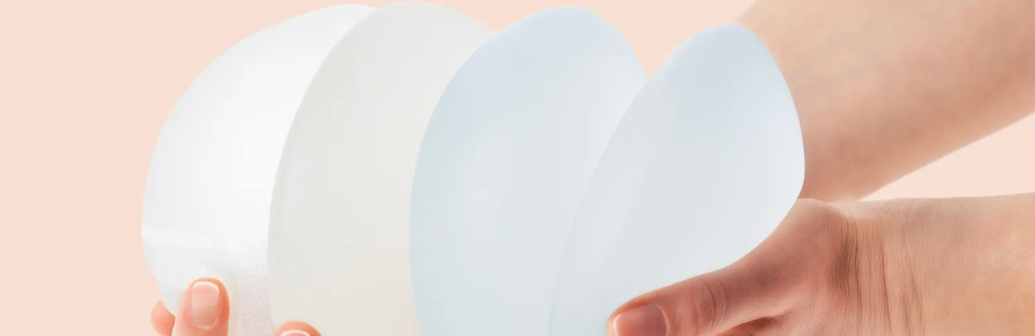 Hands holding out a stack of different types of breast implants